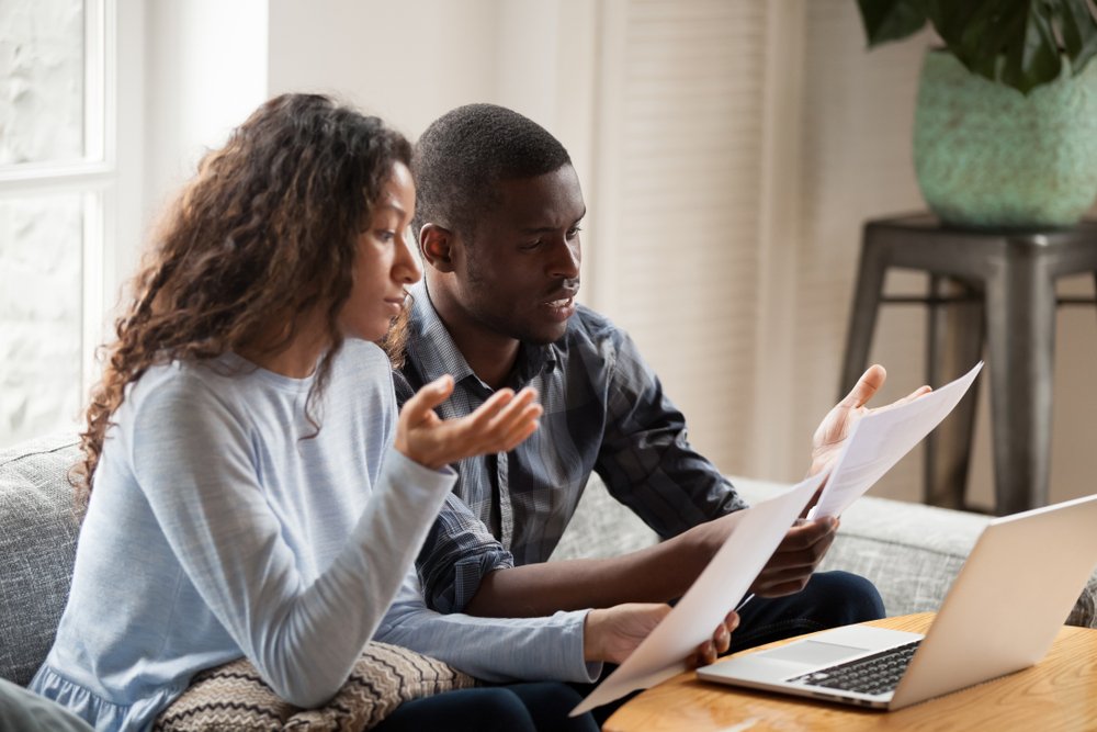 casal jovem olha para contas e simula financiamento imobiliario no laptop