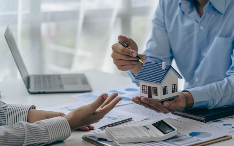 Conceito de compra de casa, corretor imobiliário com modelo de casa conversando com o cliente sobre a compra de seguro residencial e o cliente assinando contrato sob acordo formal com direito imobiliário