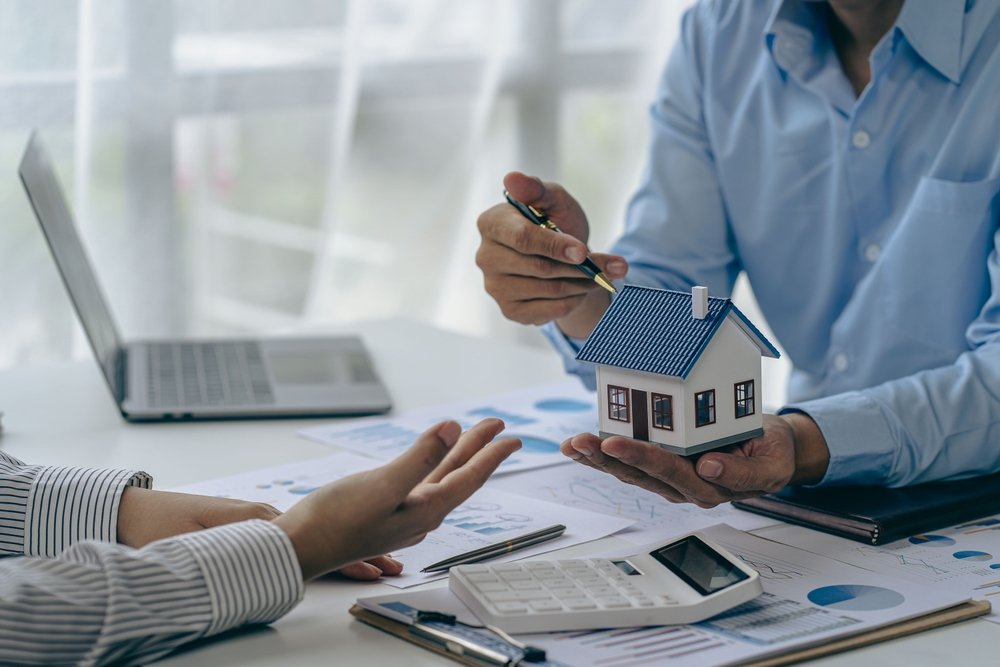 Conceito de compra de casa, corretor imobiliário com modelo de casa conversando com o cliente sobre a compra de seguro residencial e o cliente assinando contrato sob acordo formal com direito imobiliário